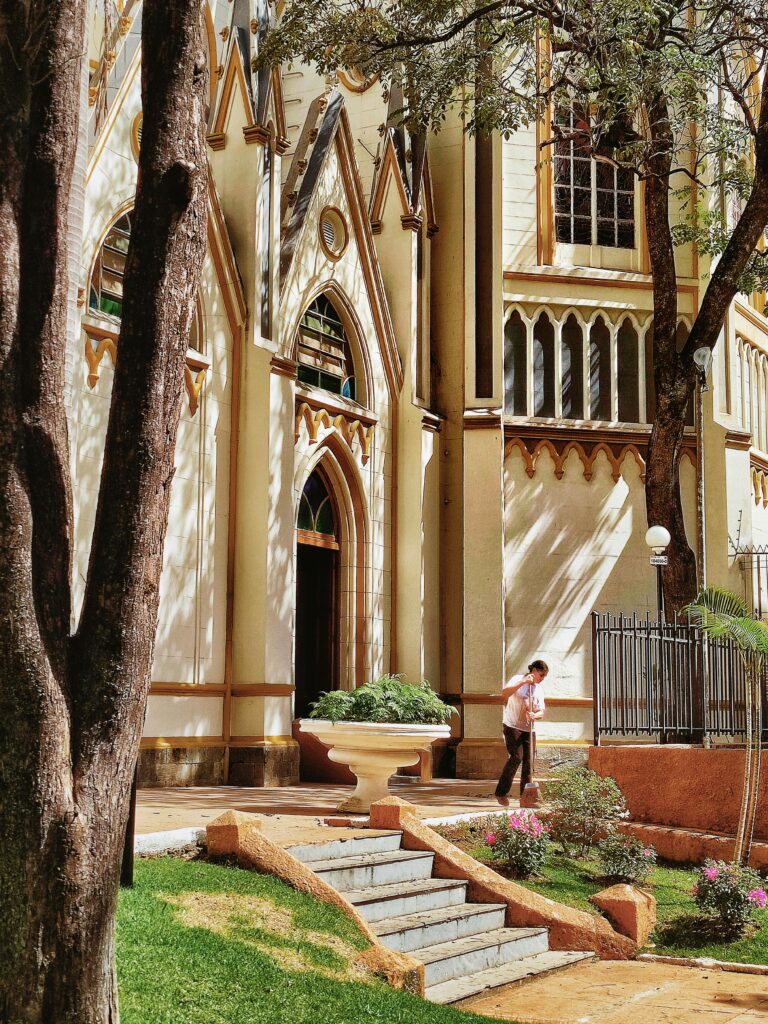 A woman cleaning outside a Catholic church in Belo Horizonte under the trees.