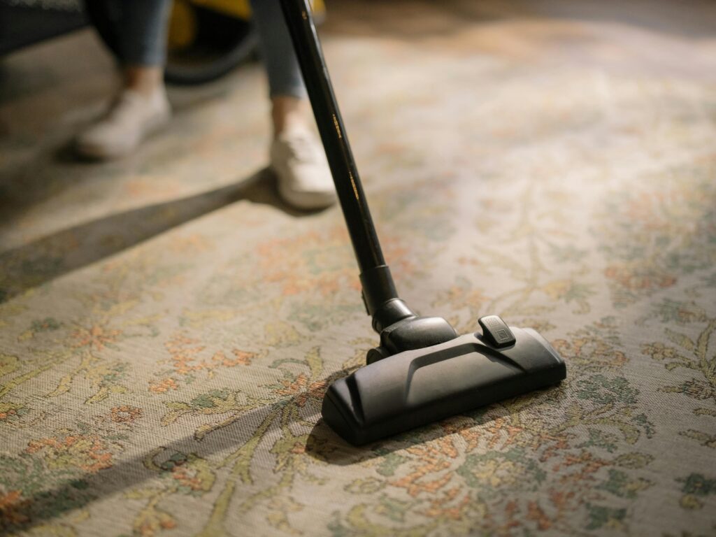 Close-up of a vacuum cleaner on a patterned carpet in a sunlit room, capturing a moment of household cleaning.