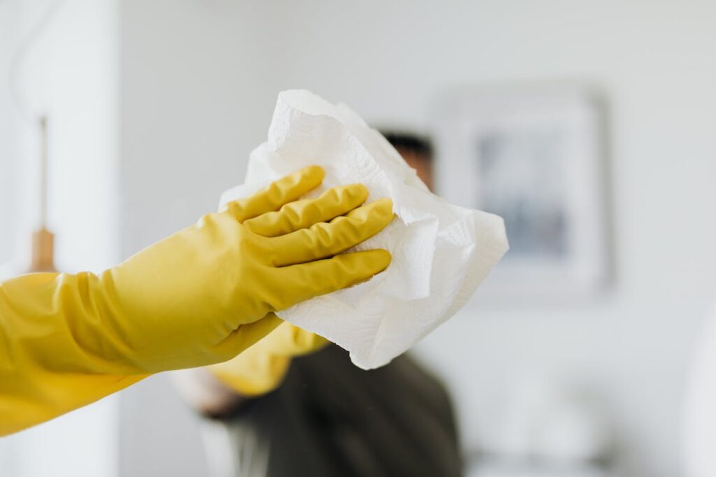 Close-up of a yellow-gloved hand cleaning a mirror with a cloth indoors.