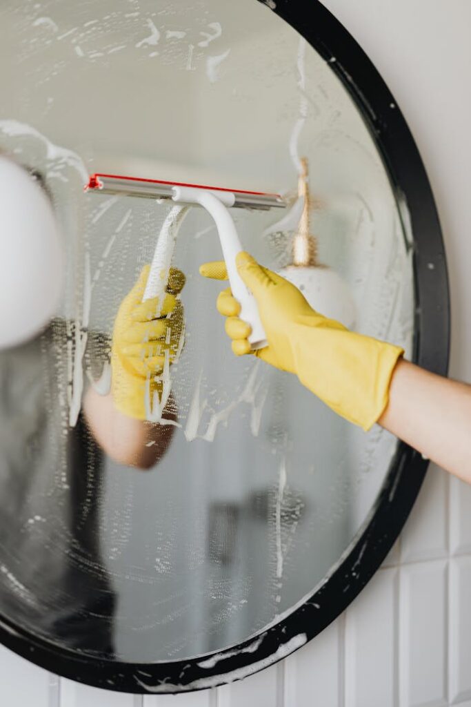 Person cleaning a bathroom mirror using a squeegee for shiny, clear results.