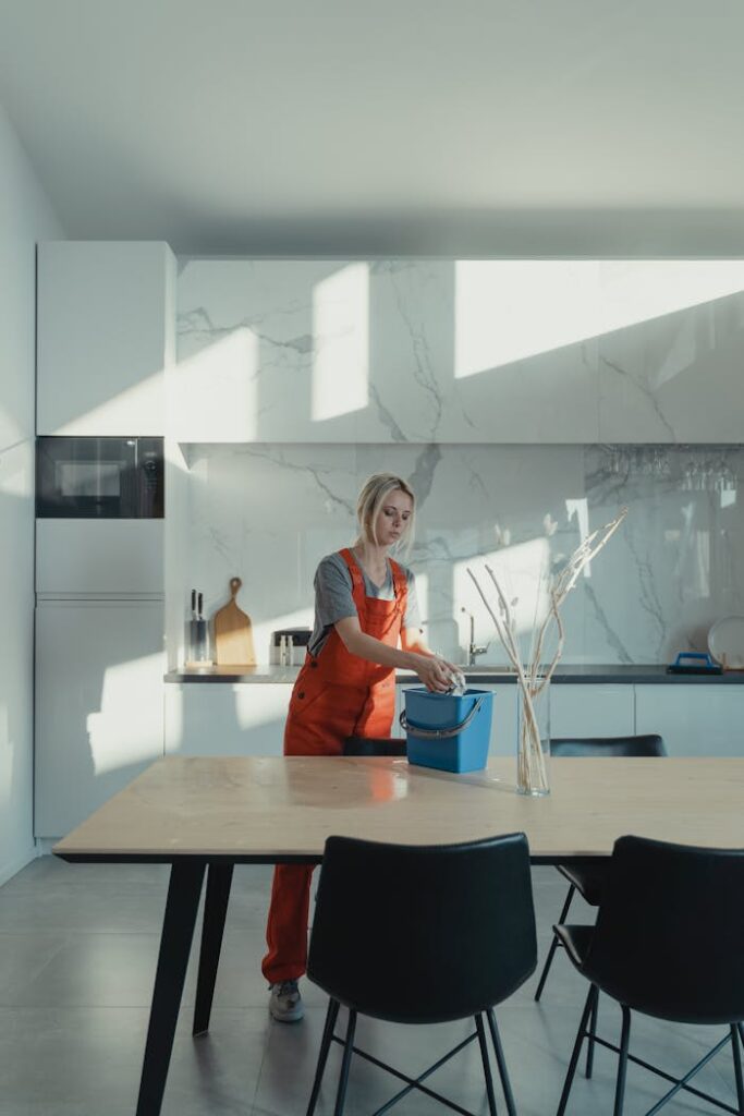 A woman in uniform cleaning a modern kitchen lit by natural light, creating a serene atmosphere.