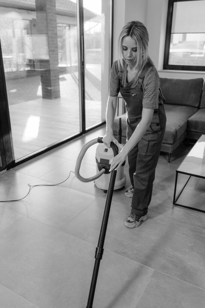 A woman in work clothes vacuuming indoors, emphasizing cleanliness and efficiency.