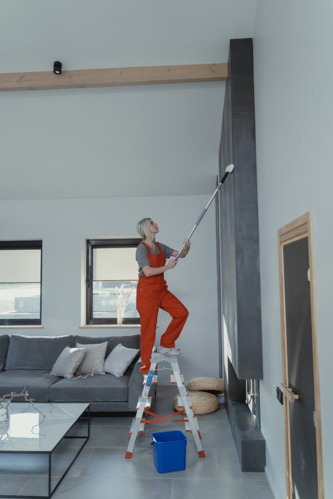 Woman in overalls on a ladder cleaning a high wall in a stylish modern living room.