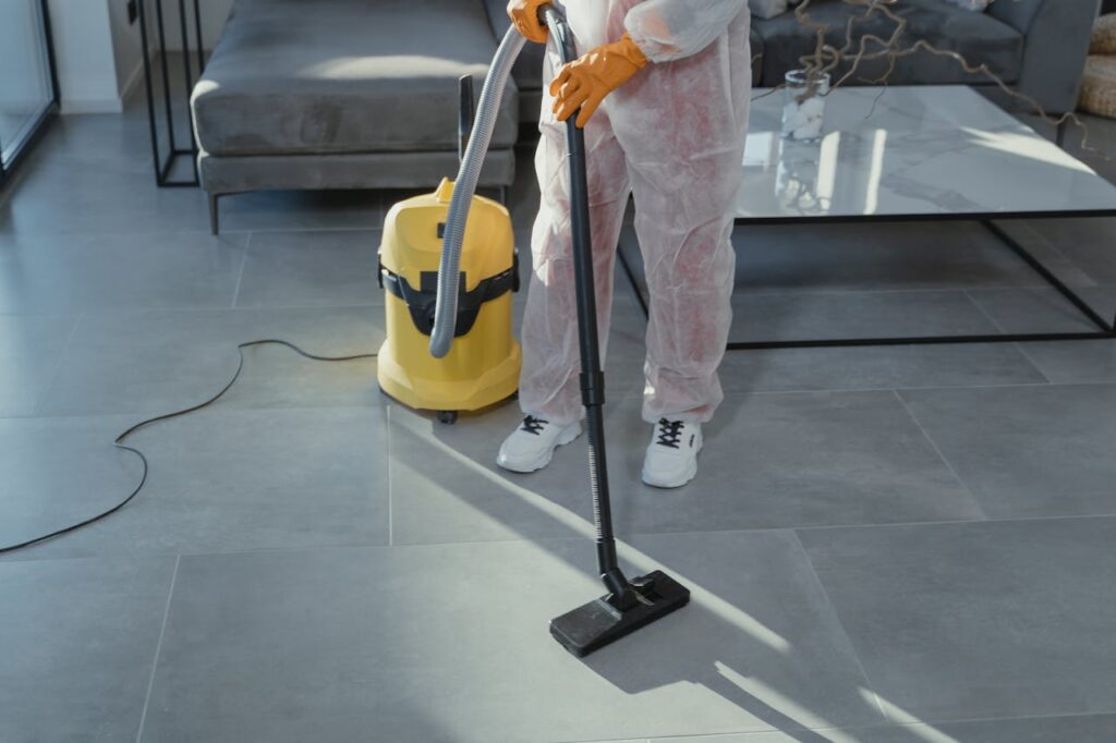 A professional cleaner in protective gear vacuuming the floor in a modern living room.