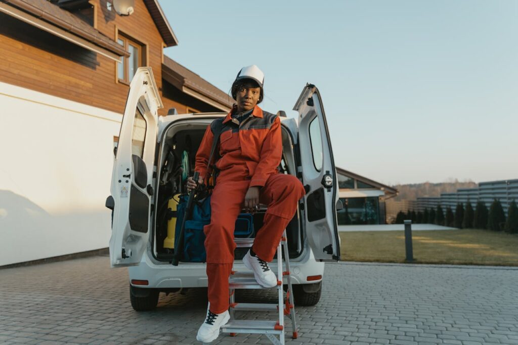 A professional worker in protective gear sits by a work van in a residential area.