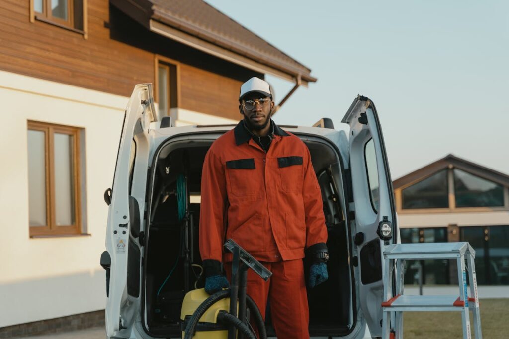 Man in workwear with cleaning equipment next to van outside a building.