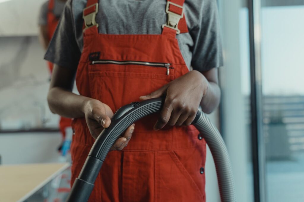 Close-up of a person in red overalls holding a vacuum hose, indoors.