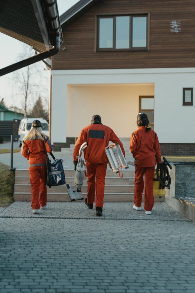 Cleaning crew in red uniforms with equipment approaching a modern house exterior.