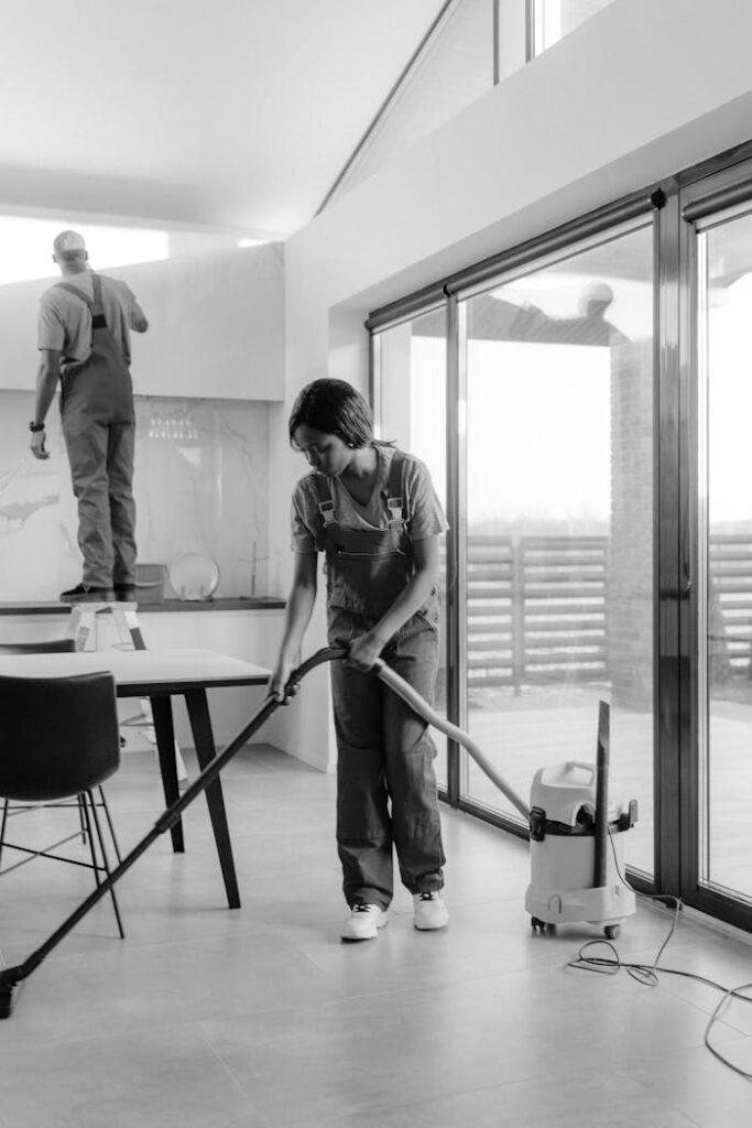 Two professional cleaners working in a modern home interior, focusing on vacuuming and dusting.