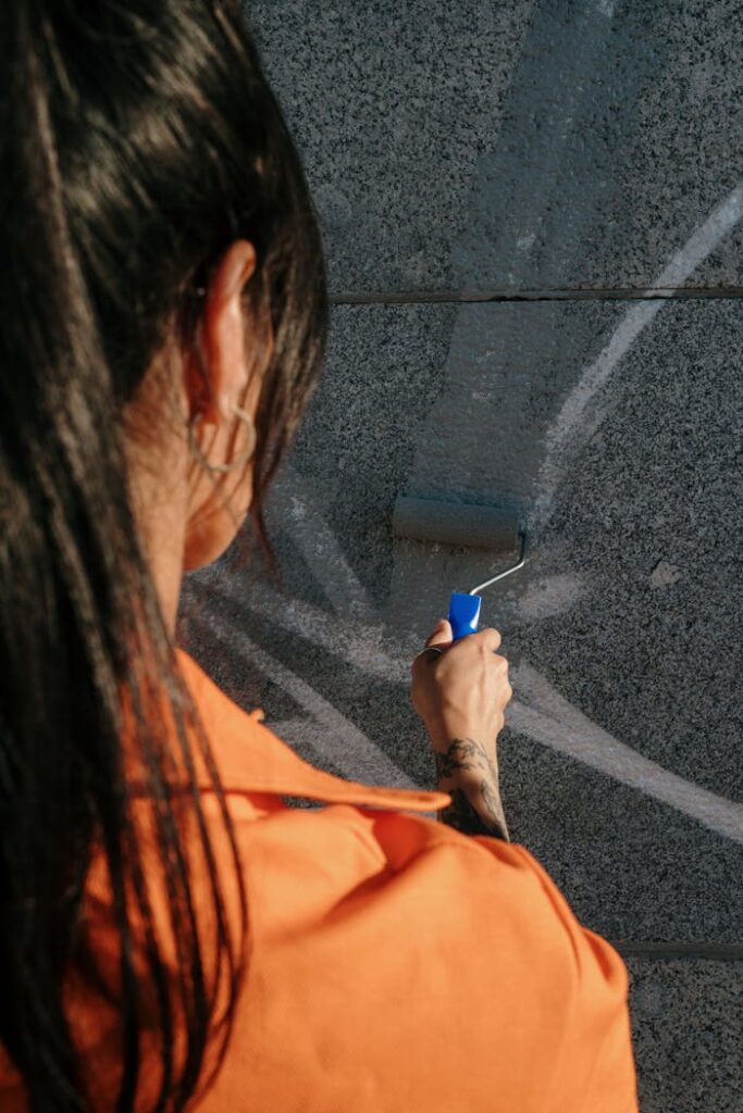 Adult woman using a paint roller to cover graffiti on a wall, engaged in community service.